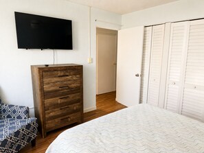 A bedroom with a bed, a wooden dresser, a television mounted on the wall, and a closet with louvered doors. - Make Memories in Paradise at Long Reef (Christiansted)
