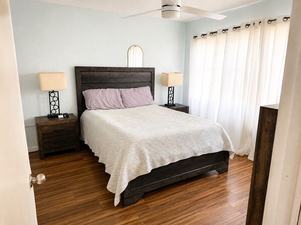 A bedroom with a bed, two bedside tables, a ceiling fan, and a window with curtains. - Make Memories in Paradise at Long Reef (Christiansted)