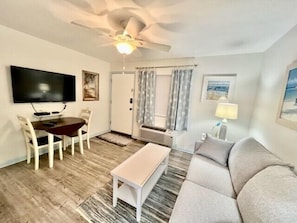 A living room with a sofa, a coffee table, a TV, and a ceiling fan. - Guest House 207 - Walk to Garden City Beach (Garden City)