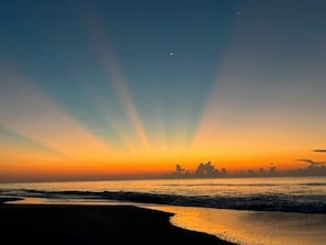 A beach scene with a sunset, waves, and a distant city skyline. - Guest House 207 - Walk to Garden City Beach (Garden City)