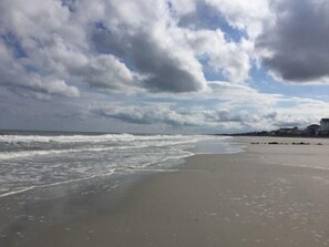 A beach with waves, a cloudy sky, and buildings in the distance. - Guest House 207 - Walk to Garden City Beach (Garden City)