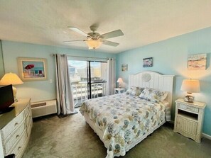 A bedroom with a bed, a ceiling fan, a window with curtains, and a nightstand with a lamp. - Guest House 207 - Walk to Garden City Beach (Garden City)