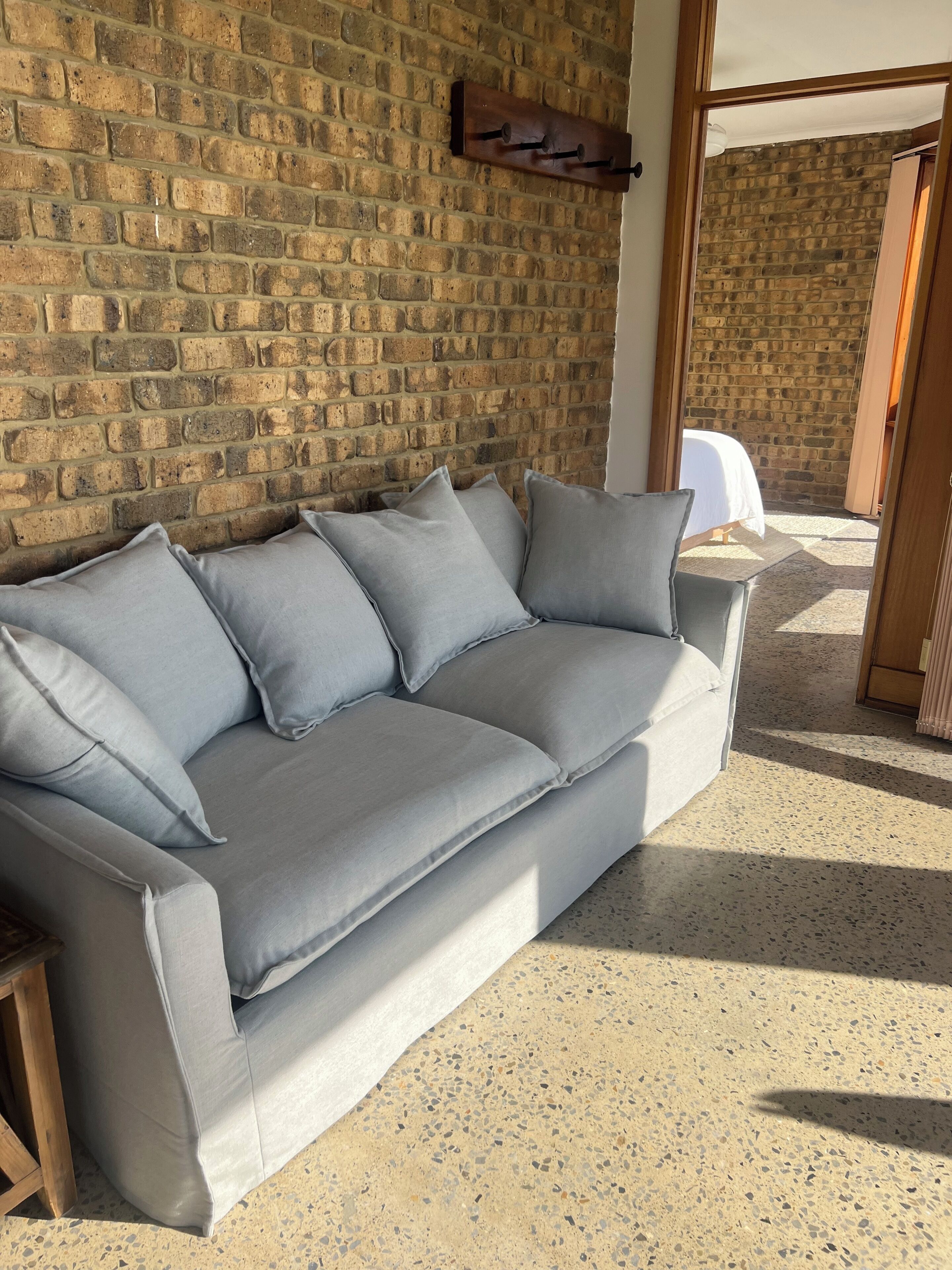 A grey sofa against a brick wall, with a small table beside it.