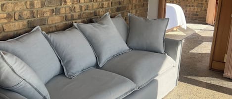 A grey sofa against a brick wall, with a small table beside it.