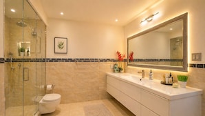 A modern bathroom with a glass-enclosed shower, a toilet, a vanity with a large mirror, and a decorative plant.