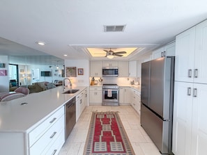 A modern kitchen with white cabinetry, stainless steel appliances, and a central island with a sink. - Artsy Waterfront Retreat - Punta Rassa 4-1003 (Fort Myers)