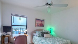 A bedroom with a bed, a desk, a chair, a window with a view, a ceiling fan, and a wall-mounted lamp. - Artsy Waterfront Retreat - Punta Rassa 4-1003 (Fort Myers)