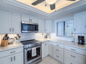A modern kitchen with white cabinetry, a built-in microwave, a stove, and a window with blinds. - Artsy Waterfront Retreat - Punta Rassa 4-1003 (Fort Myers)