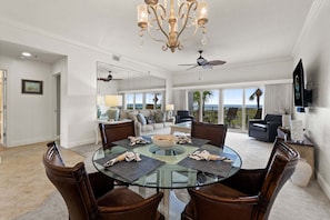 A dining area with a glass table surrounded by chairs, a chandelier, and a view of the outdoors. - New! Gulf Front! Pool, Hot Tub, Steps to the Beach, Beach Manor 210 (Miramar Beach)