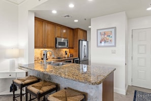 A modern kitchen with granite countertops, stainless steel appliances, and wooden cabinets. - New! Gulf Front! Pool, Hot Tub, Steps to the Beach, Beach Manor 210 (Miramar Beach)