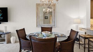 Een eetruimte met een ronde glazen tafel, zes stoelen, een kroonluchter en een grote spiegel boven de tafel.