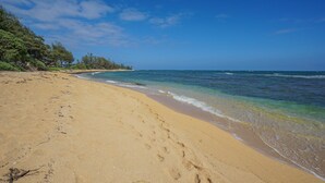 A sandy beach with footprints leading to the water, a clear sky, and a line of trees in the background. - New***Islander on the Beach 315-Top Floor Corner Mountain View with AC Sleeps 4 (Kapaa)