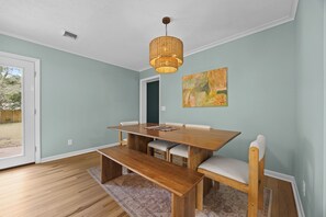 Ein Esszimmer mit Holztisch und -stühlen, einer gewobenen Leuchte und einem Bild an der Wand.