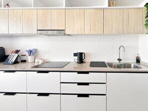 Una cocina moderna con armarios blancos, un lavamanos de acero inoxidable y una cafetera negra.