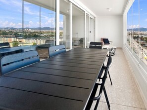 Un balcón moderno con una mesa de comedor y sillas, ventanas amplias con vistas a la ciudad y un sofá.