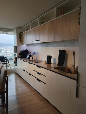 A modern kitchen with wooden cabinets, a stainless steel sink, and a view of the city. - Oceana Suites Playa Serena (Coquimbo)