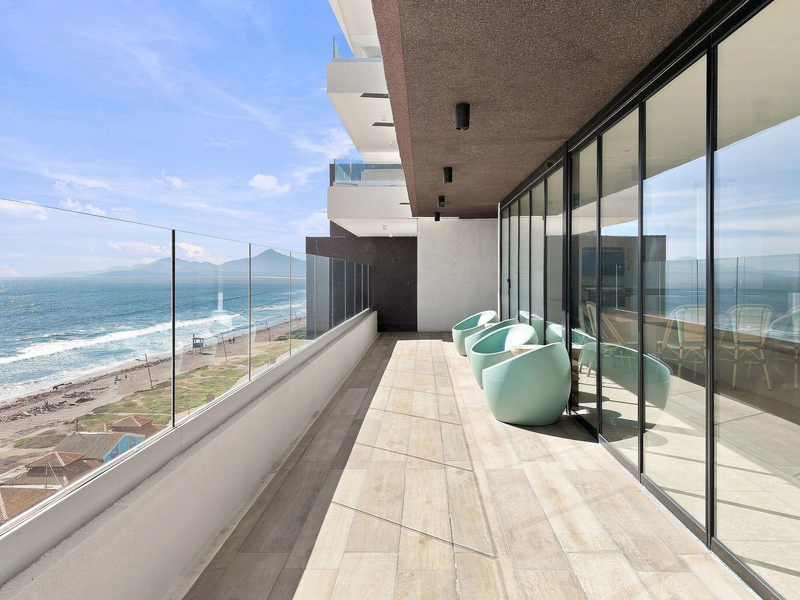 Un balcon avec vue sur l’océan, des chaises modernes et une rambarde en verre.