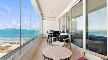 A balcony with a view of the sea, a round table, and chairs.