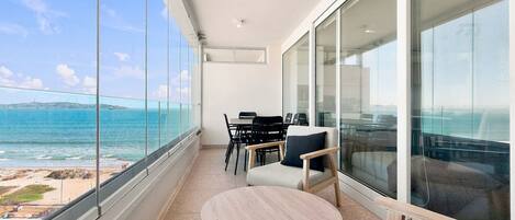 A balcony with a view of the sea, a round table, and chairs.