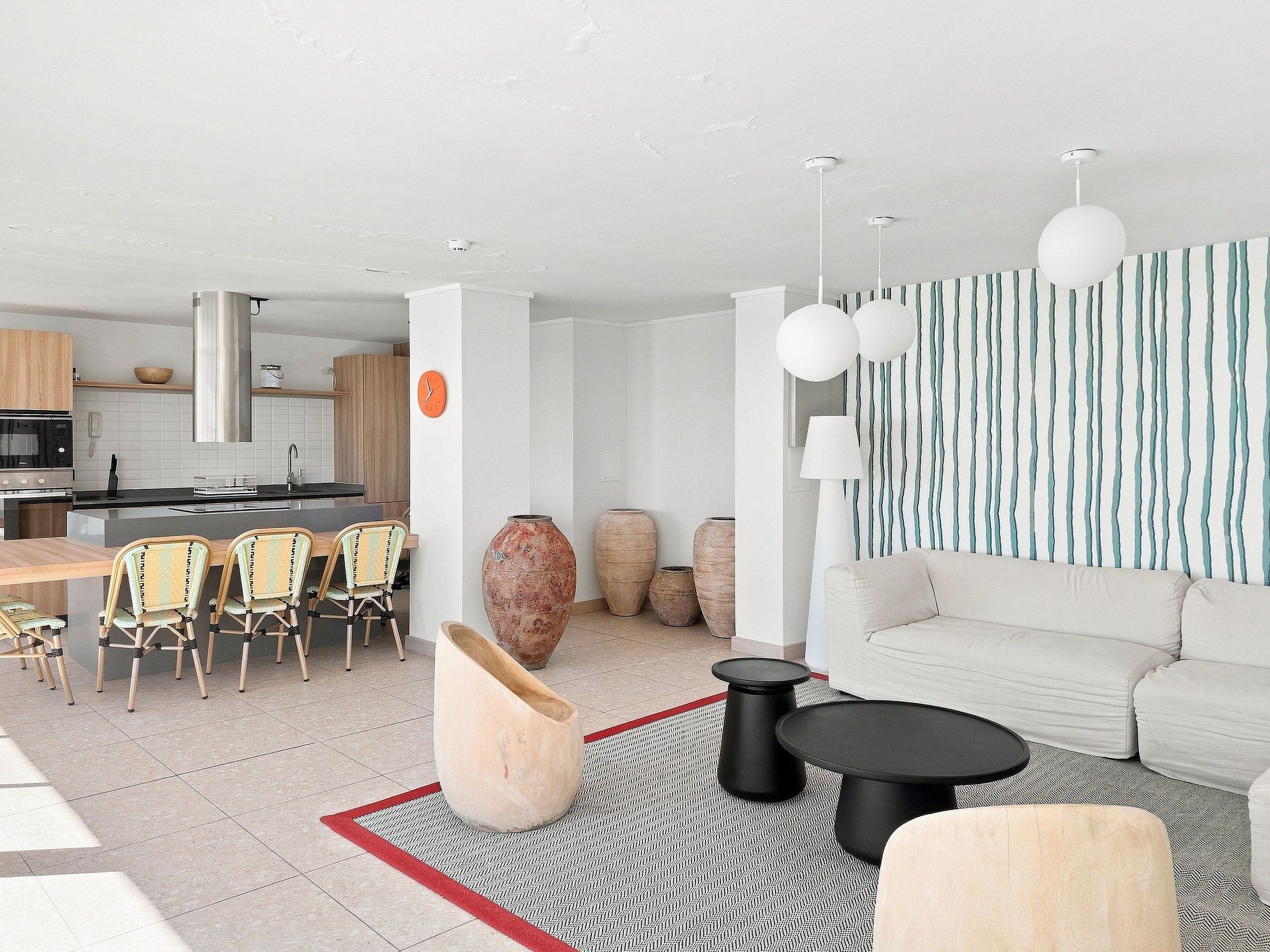 Een moderne woonkamer met een bank, salontafel en stoelen. Er is een keukenhoek met kasten en een eettafel. Sierlijke vazen en een klok zijn ook zichtbaar.