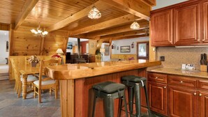 A wooden interior with a kitchen area featuring a bar, stools, and wooden cabinets. - Mountain Getaway Near Snow Summit | 4BR • 3.5BA • Game Room (Big Bear Lake)
