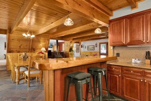 A wooden interior with a kitchen area featuring a bar, stools, and wooden cabinets. - Mountain Getaway Near Snow Summit | 4BR • 3.5BA • Game Room (Big Bear Lake)