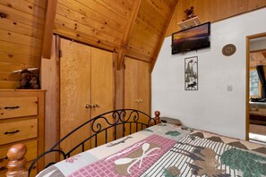 Ein Schlafzimmer mit Holzwänden, einem Bett mit gemustertem Quilt, einem Fernseher und einem gerahmten Bild eines Elchs.