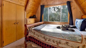 A bedroom with a wooden ceiling, a large window with curtains, a bed with a patterned blanket, and a wooden dresser. - Mountain Getaway Near Snow Summit | 4BR • 3.5BA • Game Room (Big Bear Lake)