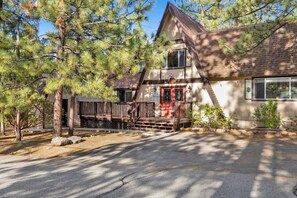 A two-story house with a wooden deck, a red door, and a stone pathway leading to the entrance. - Mountain Getaway Near Snow Summit | 4BR • 3.5BA • Game Room (Big Bear Lake)