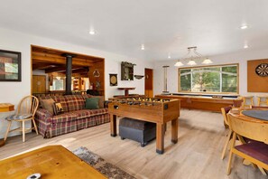 A cozy room with a foosball table, a billiards table, and a large window offering a view of the outdoors. - Mountain Getaway Near Snow Summit | 4BR • 3.5BA • Game Room (Big Bear Lake)