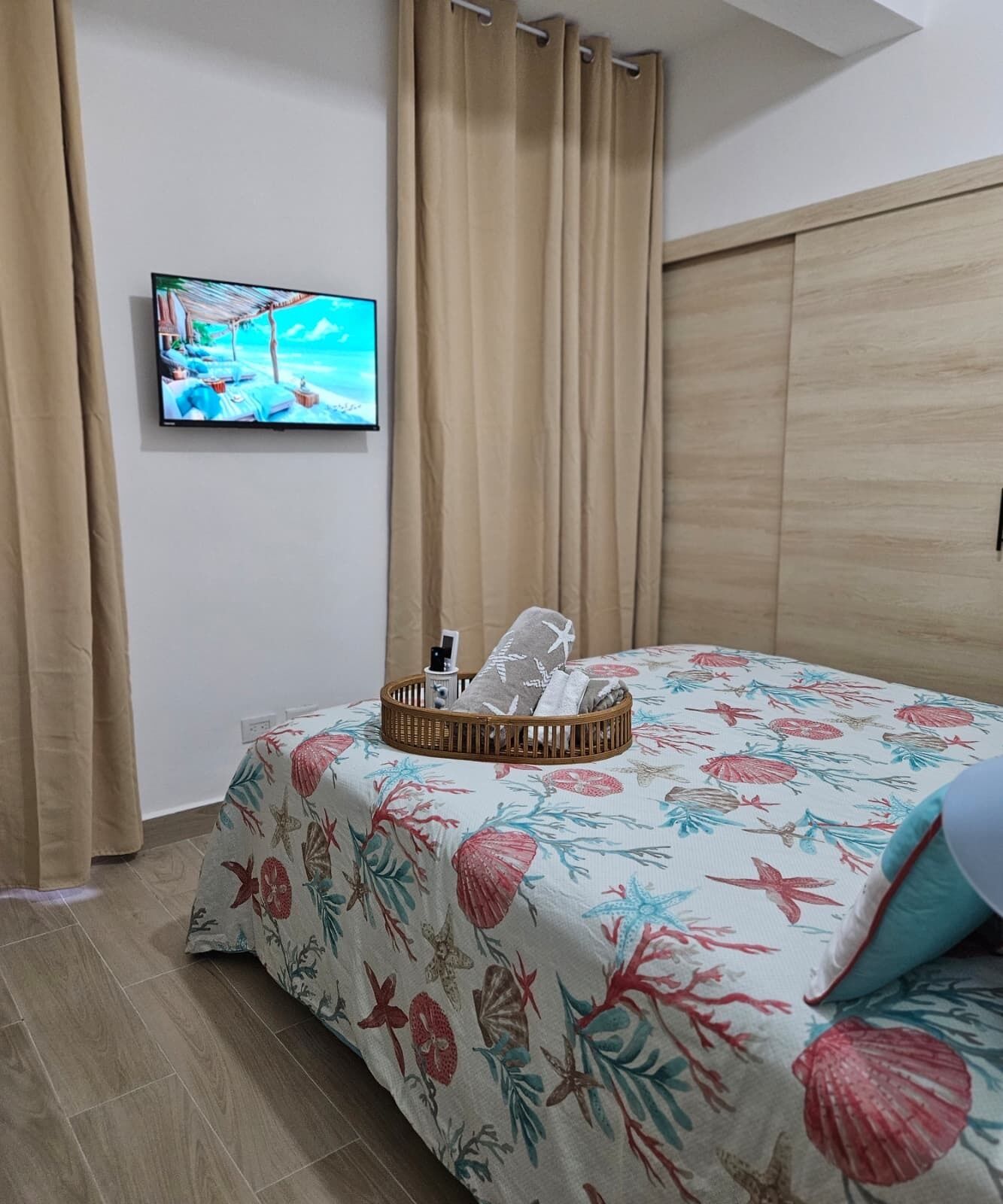 A bedroom with a bed, a television on the wall, and a window with curtains.