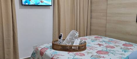 Un dormitori amb un llit, una televisió penjada a la pared i una finestra amb cortines.