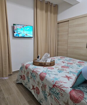 Ein Schlafzimmer mit einem Bett, einem Fernseher an der Wand und einem Fenster mit Vorhängen.