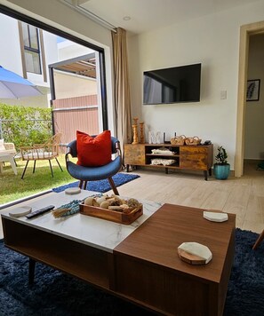 A modern living room with a sofa, a coffee table, a TV, and a view of the outdoors. - 2-bedroom townhome in peaceful Punta Cana with AC comfort (Punta Cana)
