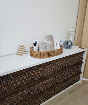 A white console table with a woven basket containing a bottle, a candle, and a starfish-patterned pillow. - 2-bedroom townhome in peaceful Punta Cana with AC comfort (Punta Cana)