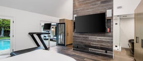 Un dormitorio moderno con una cama grande, un televisor montado en una pared de madera y un ventanal corredizo que da a un balcón.