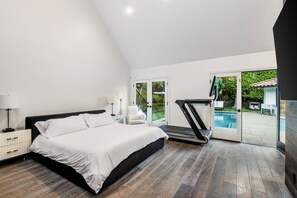 Een slaapkamer met een bed, nachtkastjes, een loopband en uitzicht op een zwembad.