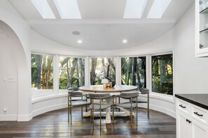 A modern dining area with a round table, six chairs, and large windows offering a view of tropical foliage. - Spacious 4-bedroom house in enchanting Beverly Hills (Beverly Hills)