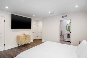 A bedroom with a bed, a dresser, a TV, and a bathroom visible through an open door. - Spacious 4-bedroom house in enchanting Beverly Hills (Beverly Hills)