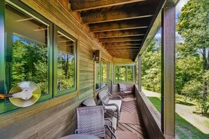 A covered porch with wooden beams, green-framed windows, wicker furniture, and a view of a wooded area. - Come Stay, Relax and Explore B8 (Killington)
