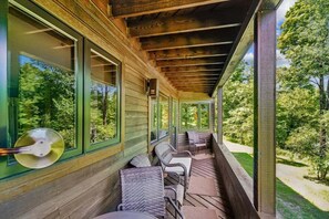 A covered porch with wicker furniture and large windows overlooking a forested area. - 2BR, 2BA Killington condo with ski-back access and winter weekend shuttle. (Killington)