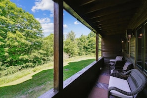 Un espacio de estar al aire libre con techo, mobiliario de mimbre y vistas a un paisaje cubierto de hierba.