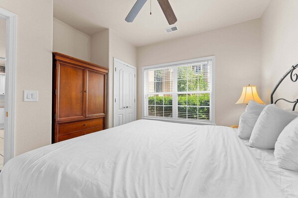 A bedroom with a large bed, a wardrobe, a window with blinds, and a lamp. - French Quarter Resort | 2 King Suites | Pet Friendly (Branson)