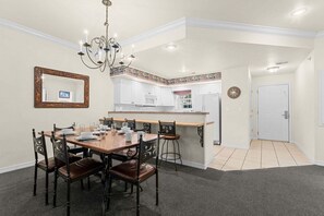 Ein Essbereich mit Holztisch und -stühlen, einer Chandelier und einer Küche im Hintergrund.