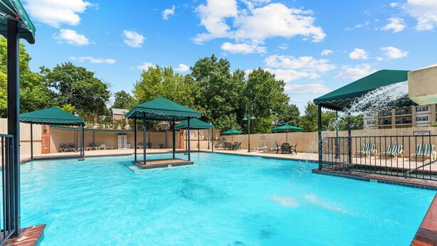 Ein Swimmingpool mit Liegestühlen und Sonnenschirmen, umgeben von einem Zaun und Bäumen.