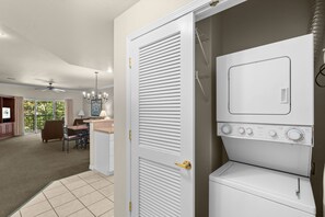 A laundry room with a front-loading washer and dryer, a ceiling fan, and a view of a dining area with a table and chairs. - 2 King Condo | Minutes to Branson Shows & Dining (Branson)