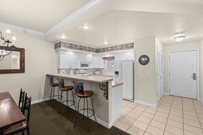 A compact kitchen with white cabinets, a central island with stools, a dining table with chairs, and a chandelier. - 2 King Condo | Minutes to Branson Shows & Dining (Branson)