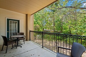 A covered outdoor area with a table and chairs, a door with a window, and a view of trees and a distant building. - 2 King Condo | Minutes to Branson Shows & Dining (Branson)