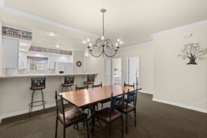 A dining area with a wooden table and chairs, a chandelier, and a kitchen in the background. - 2 King Condo | Minutes to Branson Shows & Dining (Branson)