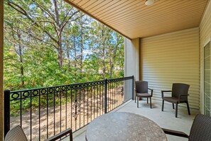 A covered outdoor area with a table and two chairs, surrounded by a metal railing, overlooking a wooded area. - 2 King Condo | Minutes to Branson Shows & Dining (Branson)